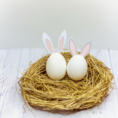 white Easter eggs with rabbit ears in the nest on a wooden table. side view