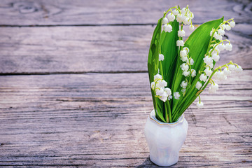 Lilies of the valley beautiful spring flowers standing bouquet in a vase on a wooden old table. Lily of the valley. Flower Spring Sun White Green Background Horizontal.