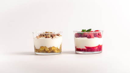 Two layered yogurt desserts. On with apple jam and pecan nuts, another with raspberry jam, fresh raspberries and mint. White background