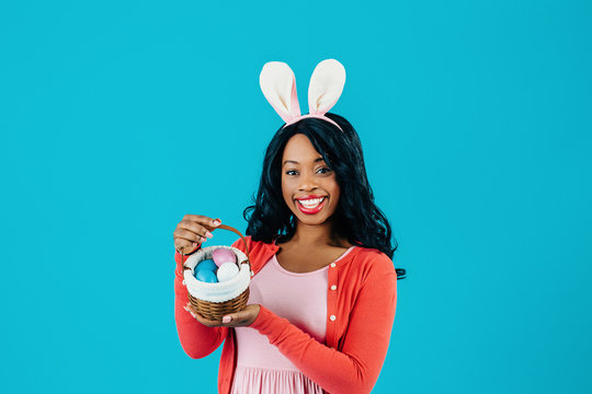 Portrait of a happy smiling mother with Easter eggs basket and bunny ears, isolated on blue background
