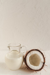 Half a coconut and a jug of coconut milk on a white background. Vegan lifestyle. Front view.