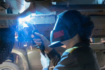 Welding work on a car, close-up. Mechanic in a welding mask welds the bottom of the car, selective...