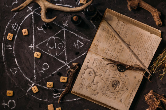 Open old book with magic spells, runes, black candles on witch table. Occult, esoteric, divination and wicca concept.