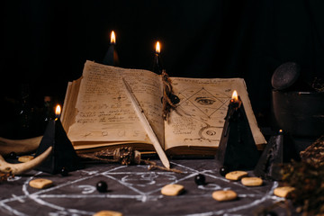 Open old book with magic spells, runes, black candles on witch table. Occult, esoteric, divination and wicca concept. - obrazy, fototapety, plakaty