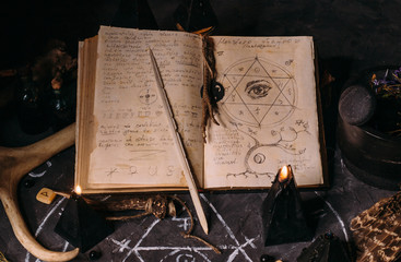 Open old book with magic spells, runes, black candles on witch table. Occult, esoteric, divination...