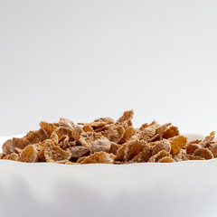 Natural whole grain wheat flakes in white bowl. Healthy breakfast concept. Plate with multigrain flakes on white background