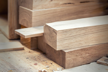 Oak wooden bar blocks materials stacked at carpentry woodwork workshop with tools and sawdust on...