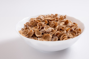 Natural whole grain wheat flakes in white bowl. Healthy breakfast concept. Plate with multigrain flakes on white background
