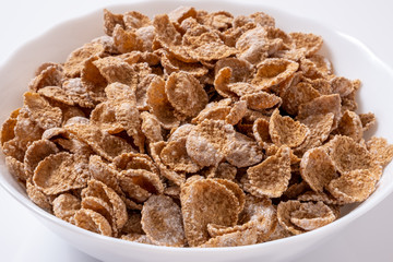 Natural whole grain wheat flakes in white bowl. Healthy breakfast concept. Plate with multigrain flakes on white background