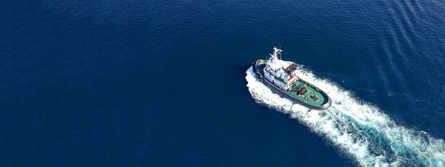 Aerial drone ultra wide top down photo of tug assisting boat cruising near Asian destination port