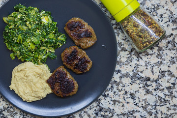 A plate of steamed spinach with cottoge cheese, humus and turkish meatballs with spices. Healthy diet concept.