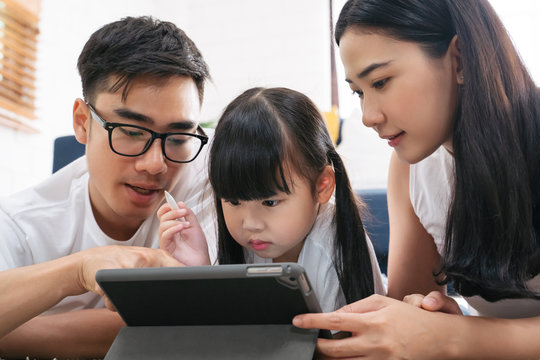 Asian family spending time together in living room. Daughter using tablet learning education technology with family together.