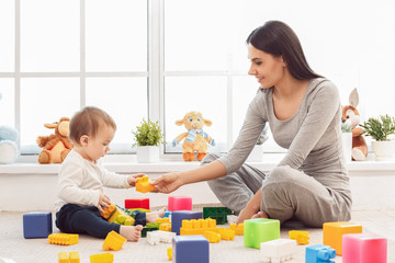 Motherhood. Mother and son sitting on floor playing with bricks smiling joyful