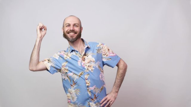 Funny dance of a man wearing hawaiian shirt. Cheerful bearded bald man dancing and having fun on white background.