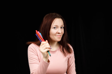 Cute woman holds markers or pens in her hand and shows on a black background. Copy space for text