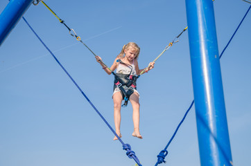 lovely blond caucasian girl jumping in the jump attraction in the playground