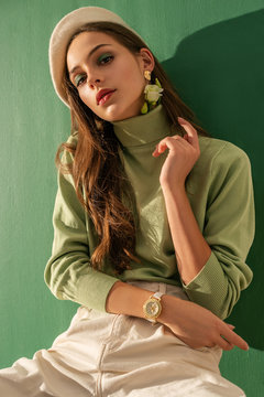 Young Beautiful Fashionable Woman Wearing Green Turtleneck, White Beret, Wrist Watch, Posing On Mint Color Background. Spring Fashion Concept