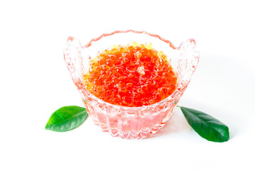 Red salmon caviar in a glass caviar bowl is decorated with green leaves on a white background