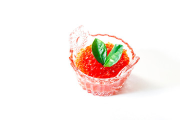 Red salmon caviar in a glass caviar bowl is decorated with green leaves on a white background
