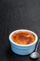 Creme brulee in blue porcelain pot on black stone background
