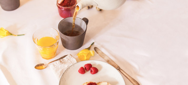 Easter table laid for Easter breakfast with narcissus flowers, hot tea and orange juice and raspberry jam silver cutlery natural and sustainable decoration.