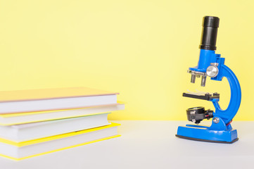 Microscope in blue on a yellow background with books on a white table. Advertising concept for a store of children's educational products.