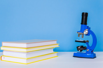 Microscope in blue on a blue background with books on a white table. The concept of learning at school, research.