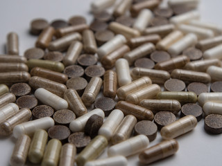 many different pills and capsules of different colors on a white table, side view