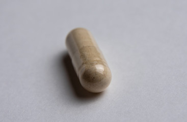 one capsule lies on a white background, illuminated from the side