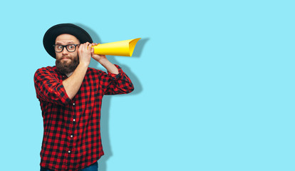 Handsome hipster guy secretly listening through yellow tube rolled up paper. Your text here! Discount, sale, season sales.