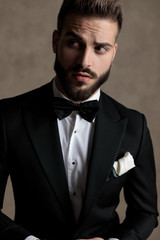 Charming groom looking away curiously while wearing tuxedo