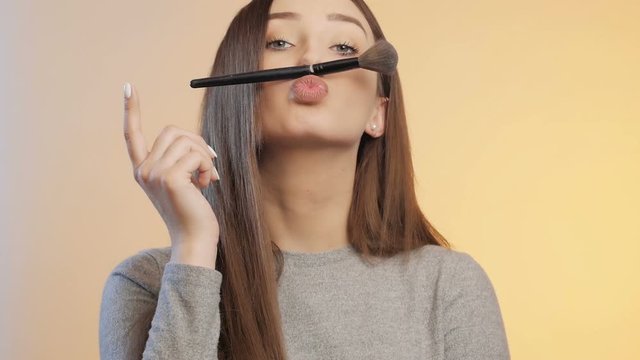 funny girl grimaces and fooling around with a makeup brush on a colored studio background, young woman in a positive mood, female beauty concept