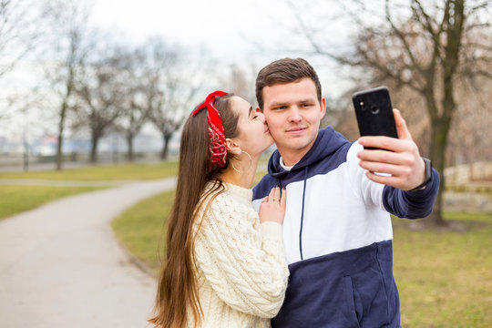 Loving cheerful happy couple taking selfie in the city. Capturing happy moments together. Image of young happy woman kissing and hugging beautiful man. Woman and man traveling on romantic vacation