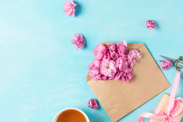 Festive or wedding composition. Spring pink blossom flowers in envelope with cup of tea and gift box on blue background
