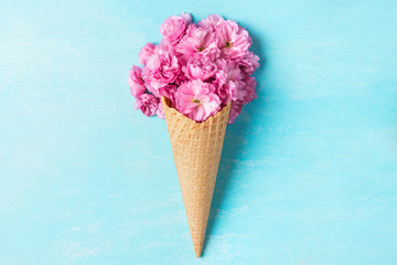 Ice cream cone with spring blossom pink cherry or sakura flowers on blue background. Minimal spring concept. Flat lay.