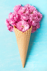 Spring pink cherry blossoming flowers in waffle cone on blue background. Minimal spring concept. flat lay. top view