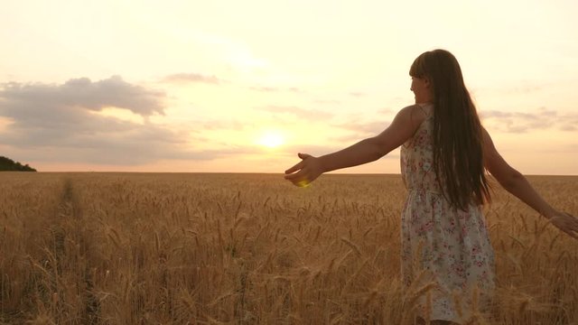 happy young girl runs in slow motion across field, touching ears of wheat with her hand. Beautiful free woman enjoying nature in warm sunshine in a wheat field on sunset background. girl travels.