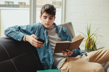 young teenage boy with mobile phone and books at home or apartment