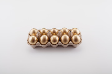 A dozen Golden eggs in a cassette top view, on a white background. The concept of Easter, abundance and preservation of Finance.