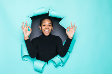 Young smile latin woman with okay gesture posing from green paper hole