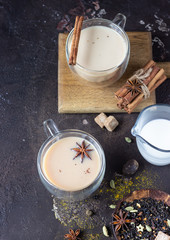 Traditional masala chai in glass cup with ingredients (cinnamon, anise, cardamom, nutmeg, pepper...