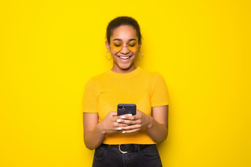 Photo of latin young woman chatting by mobile phone isolated over yellow background.