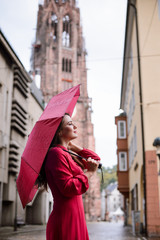 Girl with red umbrella having a walk in old town, dreaming of someone