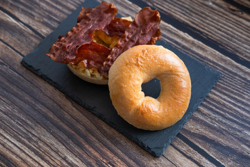 Bacon and scrambled eggs bagel on a slate plate in wooden background.  Close up view.