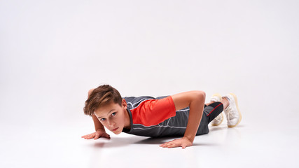 Fototapeta na wymiar Pushing limits. Full-length shot of a teenage boy engaged in sport, looking at camera while doing push-ups. Isolated on white background. Training, active lifestyle concept