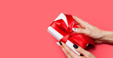Gift box with a bow in the hands of a woman on a red background. Copy space © Alina