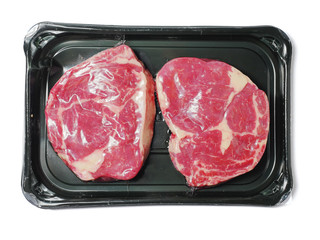 Two fresh premium rib eye steak in a vacuum pack package on a white background.