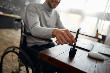 Fototapeta premium Cropped photo of young designer in a wheelchair using stylus pen and digital tablet while working in the modern office. Design studio