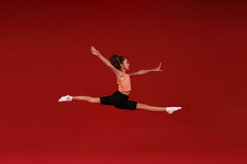 Fototapeta na wymiar Be the Best. A cute kid, girl is engaged in sport, she is in motion jumping over in the air. Isolated on red background. Fitness, training, active lifestyle concept. Horizontal shot