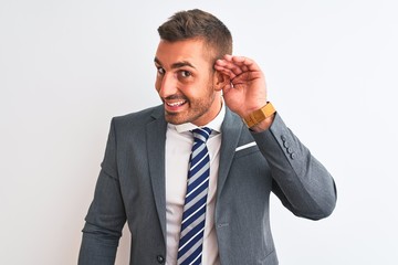 Young handsome business man wearing suit and tie over isolated background smiling with hand over ear listening an hearing to rumor or gossip. Deafness concept.